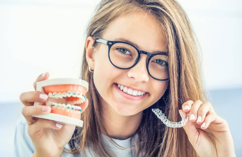 Dental invisible braces or silicone trainer in the hands of a young smiling girl. Orthodontic concept